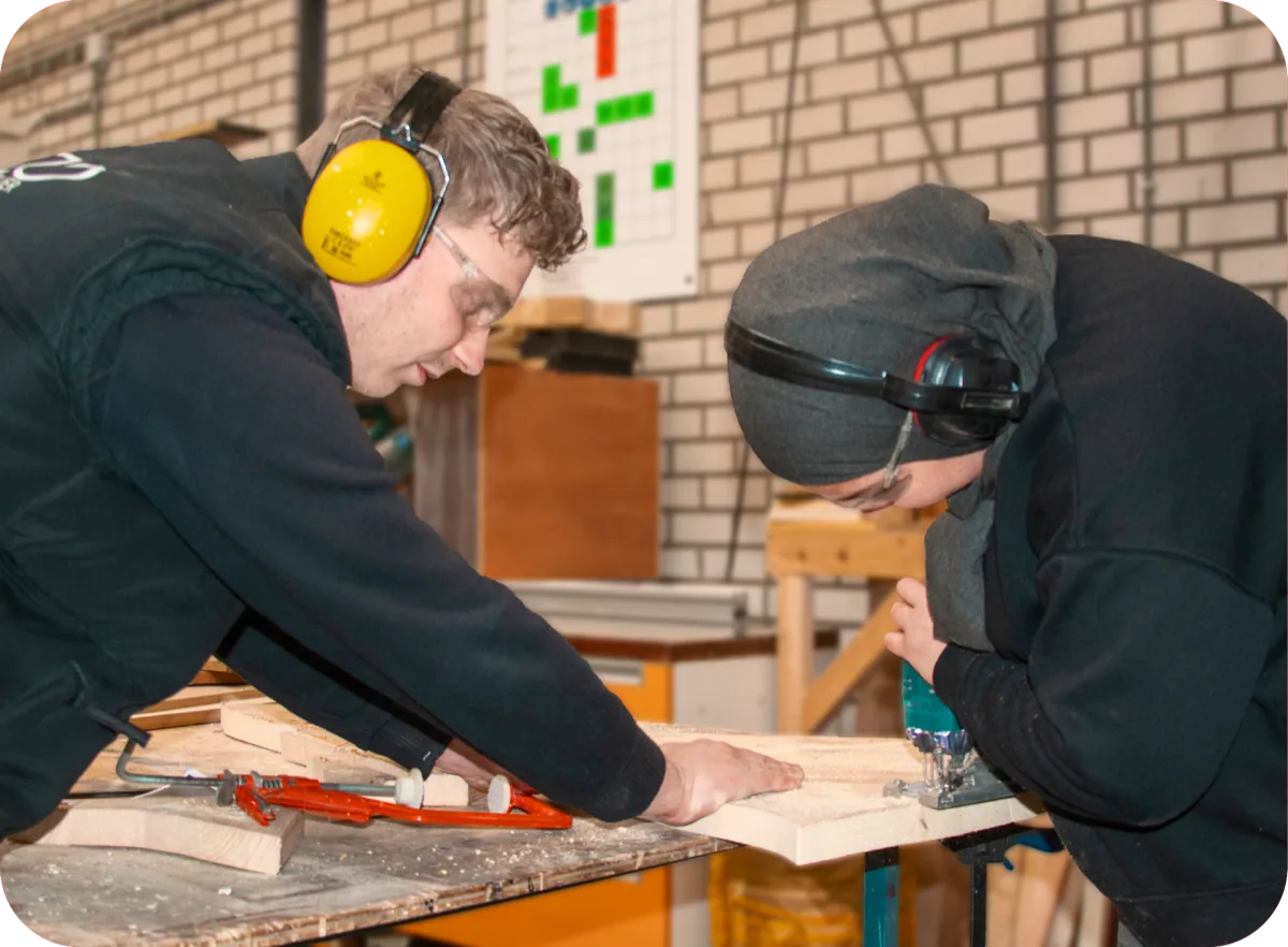 Twee deelnemers werken aan een houten plank